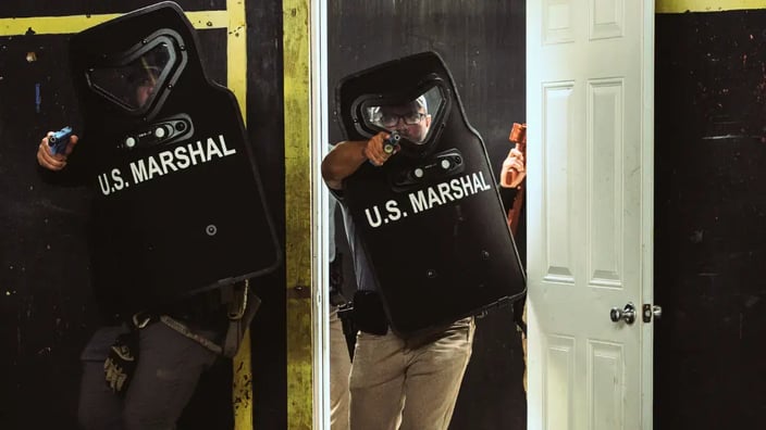 Two tactical operators using ballistic shields marked "U.S. MARSHAL" conducting a shielded entry during CQB training.