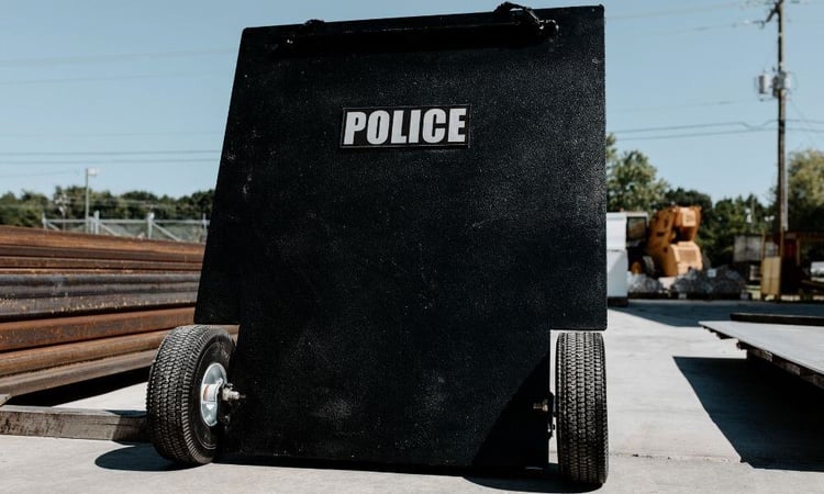 A mobile ballistic shield used by police, equipped with wheels for easy maneuverability during tactical operations.