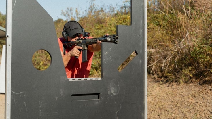 Shooter aiming through multi-port training barricade during a firearms drill on an outdoor range